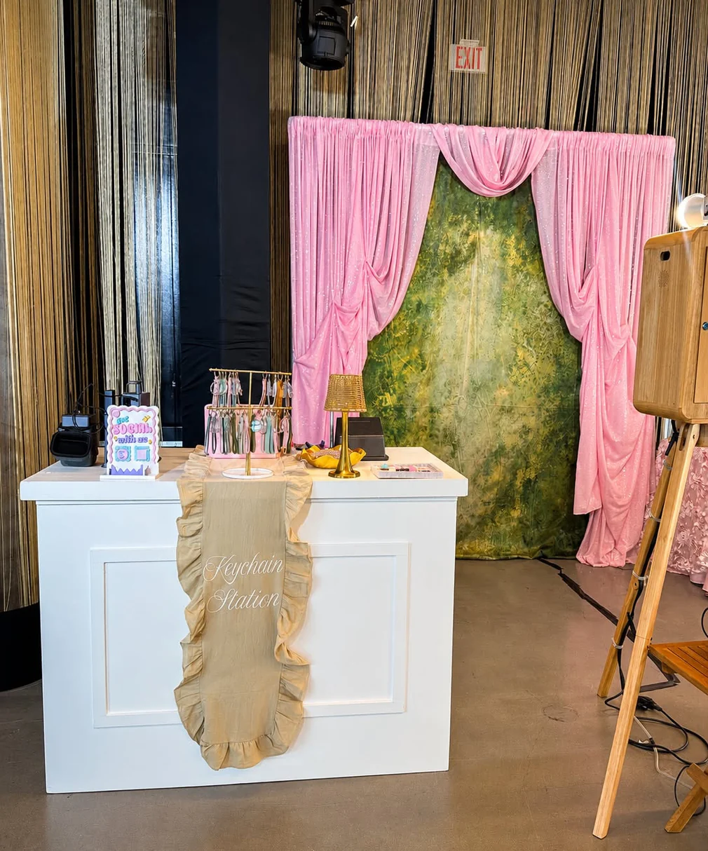 The Keychain Station bar with photo keychains on a charm rack, set up in front of a pink draped backdrop.