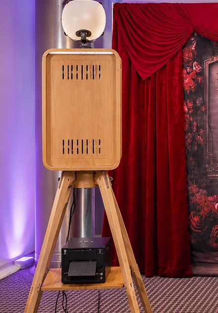 Photo booth on a wooden tripod with its printer on the shelf below.