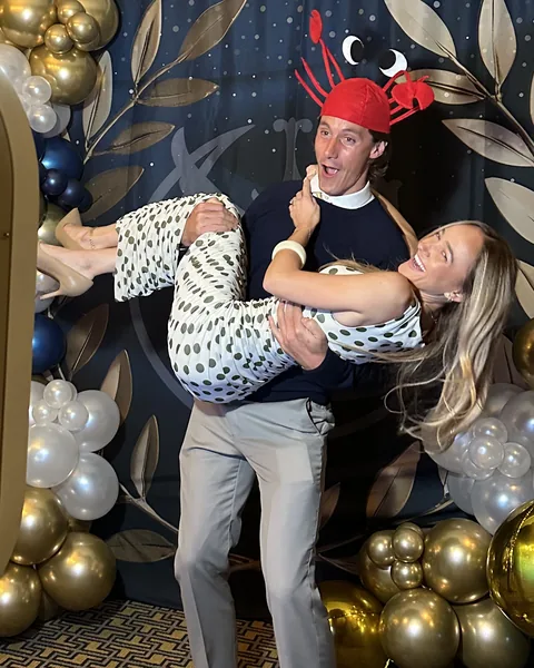 Two guests laughing in front of a balloon and foliage backdrop.