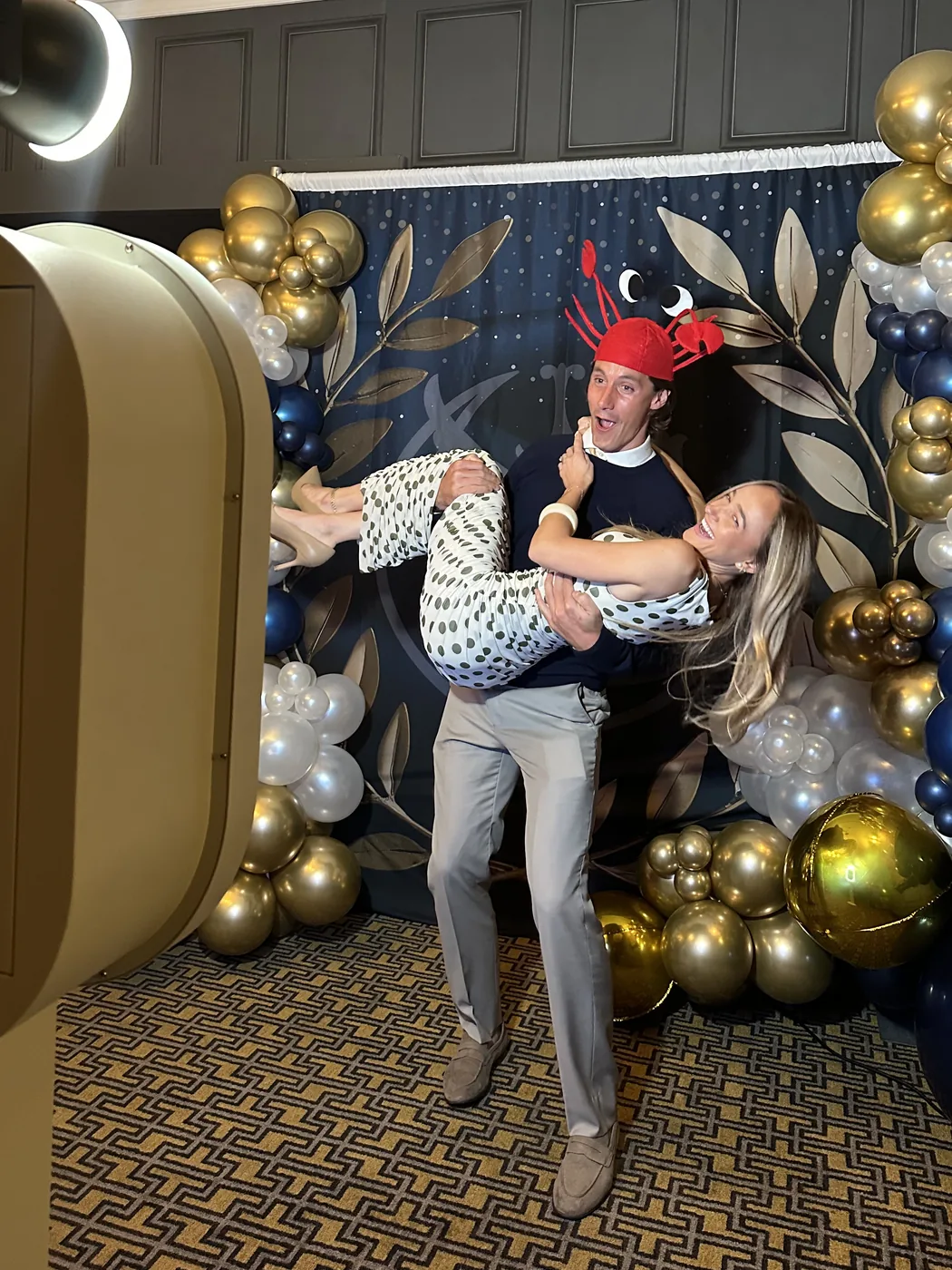Two guests laughing beside the open air booth in front of a balloon backdrop.