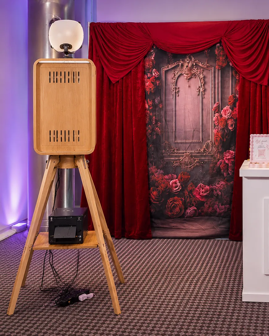 The booth with its photo printer on the shelf below, in front of a red velvet and rose backdrop.