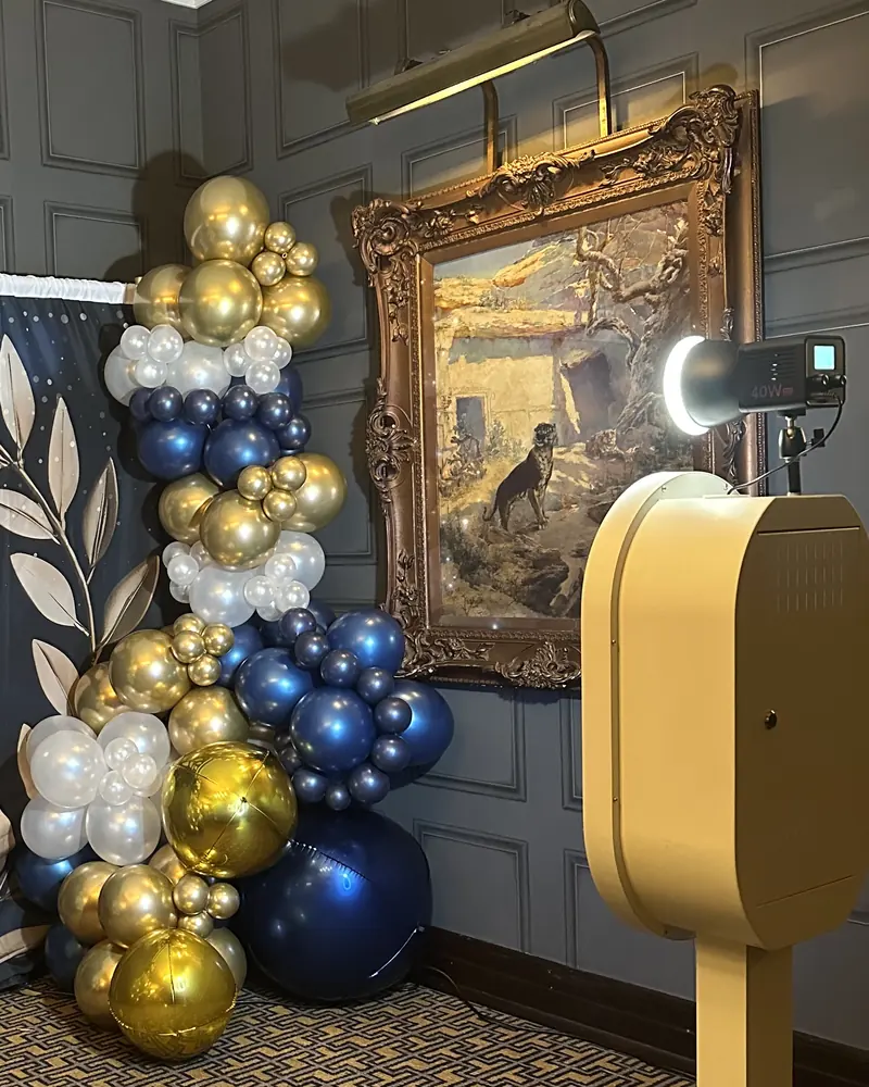 The booth set up in a panelled event room beside a navy and gold balloon garland.