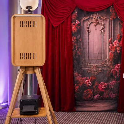 The open air photo booth and its photo printer set up beside a red velvet backdrop.