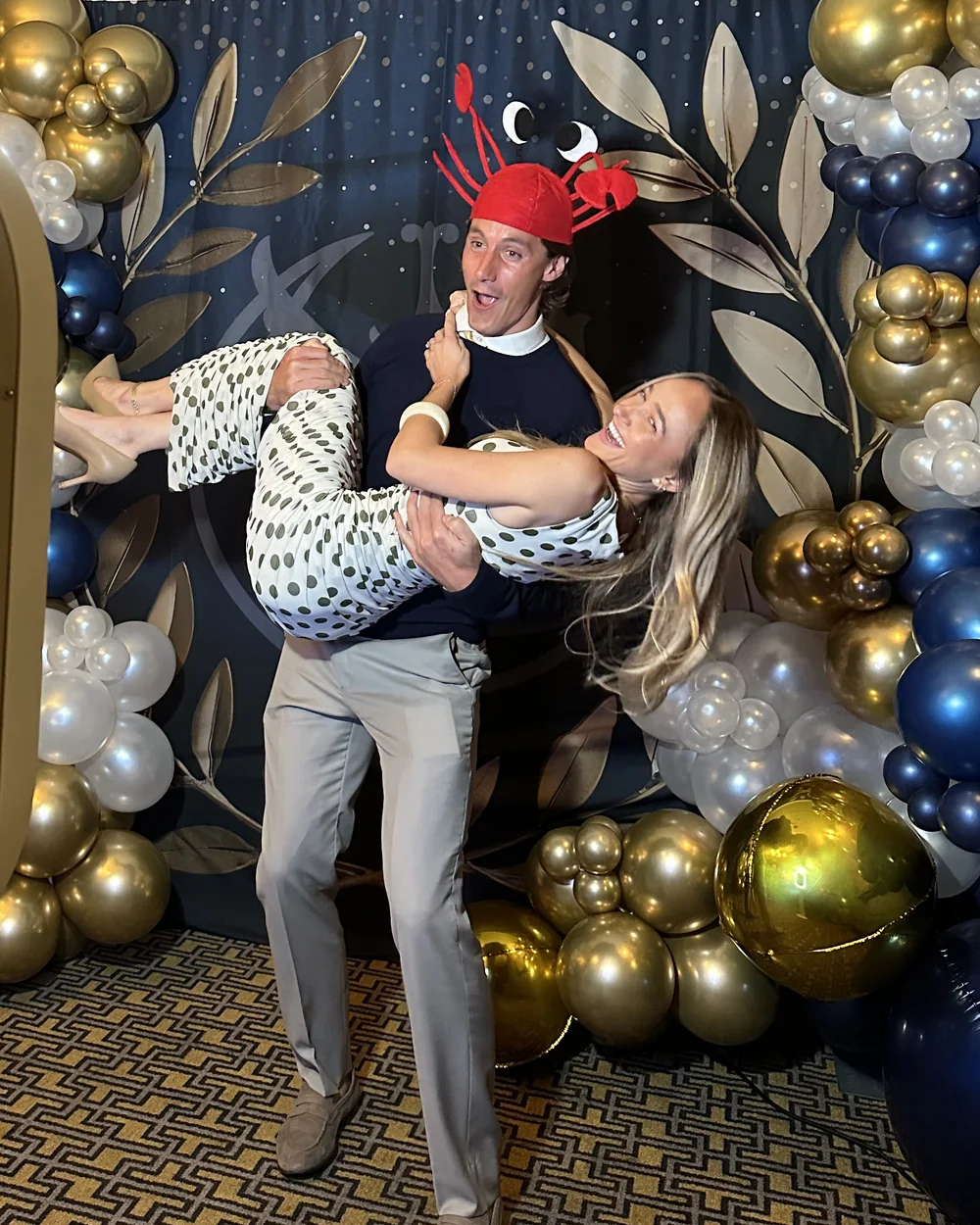 Two guests laughing as one lifts the other in front of the photo booth backdrop.