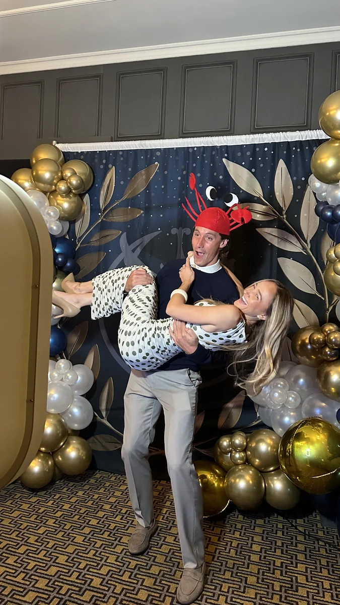 Two guests laughing in front of the photo booth backdrop, one carrying the other.