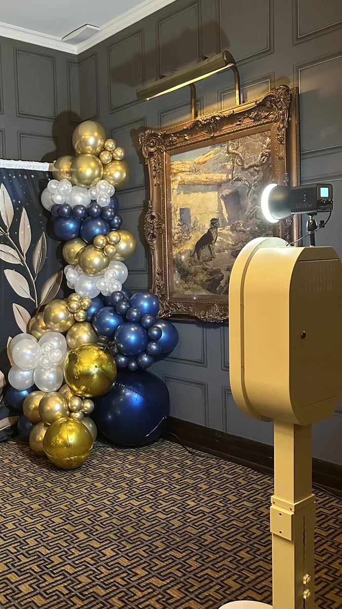 The open air photo booth lit and ready beside a navy and gold balloon garland.