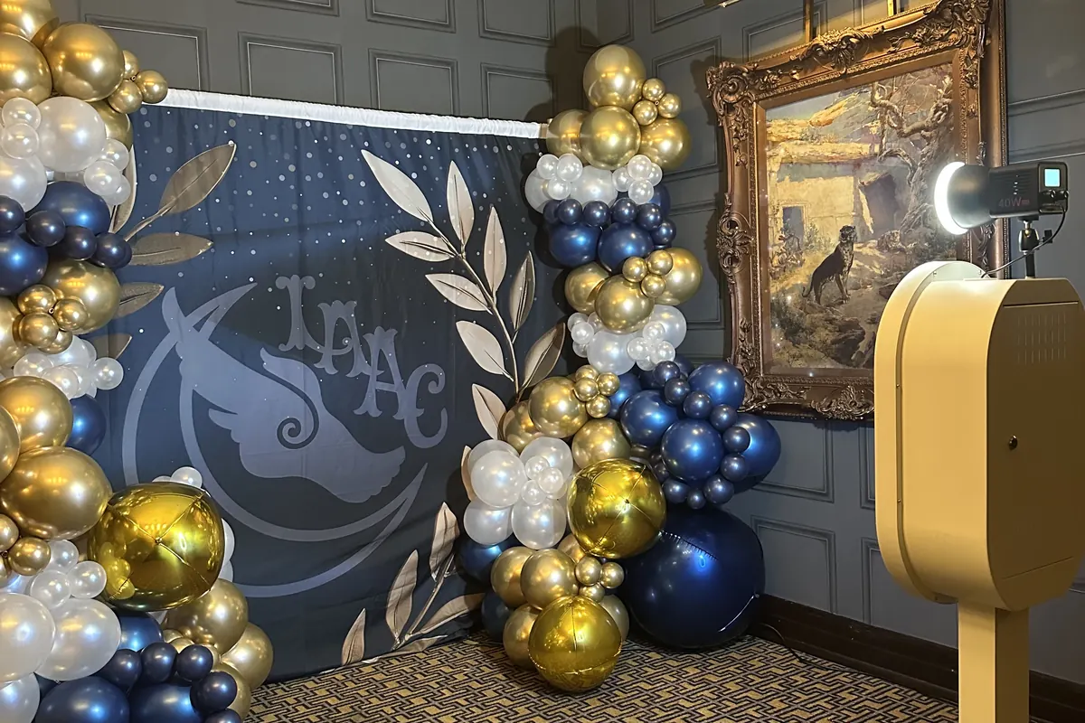 The open air booth beside a navy and gold balloon garland in a panelled event room.
