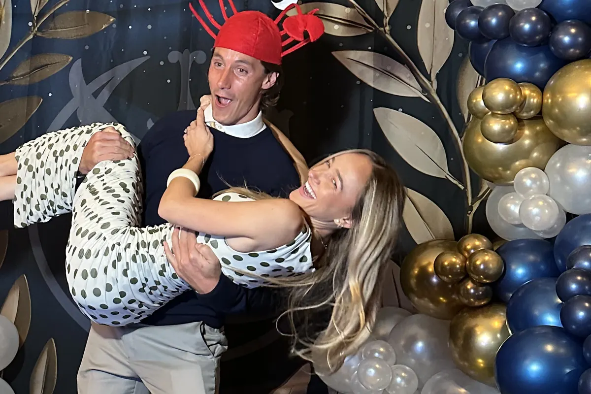 Two guests laughing in front of the booth's balloon and greenery backdrop.