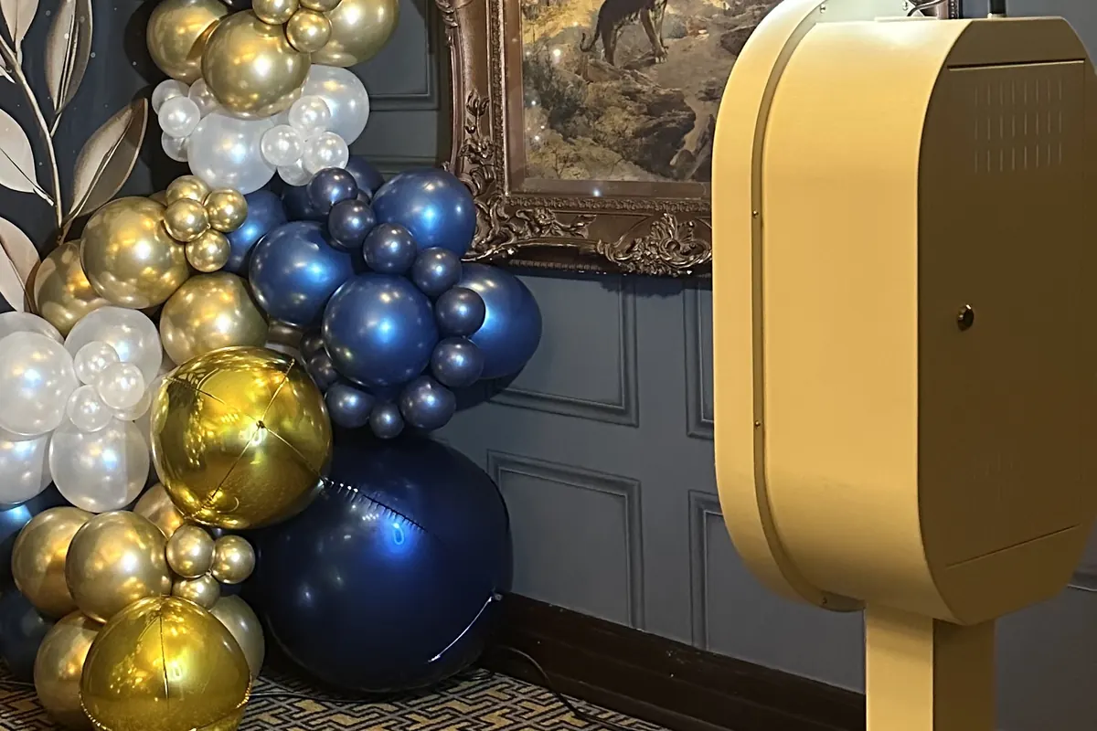 The booth on its slim stand against the wall beside a balloon garland.